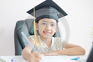 Little Asian girl wearing graduate hat doing homework and smile with happiness for success of education concept select focus