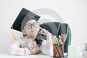 Little Asian girl wearing graduate hat hugging clear glass jar piggy bank and smile with happiness for money saving to wealthness