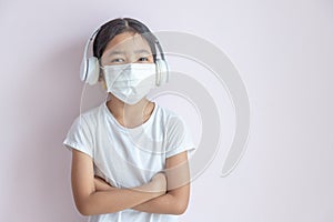 little Asian girl wearing a medical protective mask and earphones
