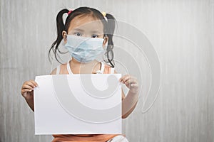 Little asian girl wearing surgical mask while holding blank white paper.