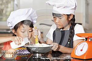 Little asian girls pour milk into wheat flour and egg