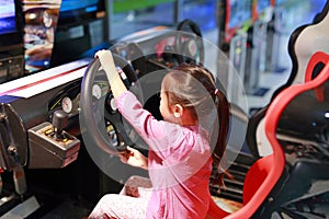 Little Asian kid girl playing arcade video game. Racing car