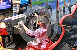 Little Asian kid girl playing arcade video game. Racing car