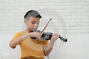 A Little Asian kid playing and practice violin musical string instrument against in home, Concept of Musical education,