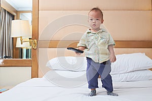 Little Asian toddler baby boy child holding the tv remote control and watching television in bedroom