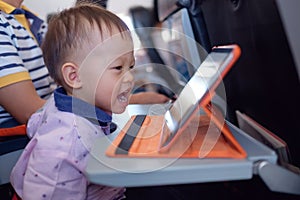 Little Asian toddler boy coloring in coloring book with crayons during flight on airplane