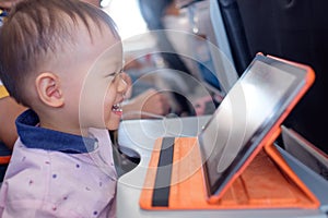 Little Asian 1 year old toddler boy coloring in coloring book with crayons during flight on airplane