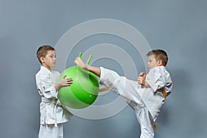 Little athlete in white karategi kicks a green ball