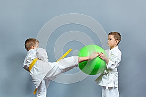Little athlete in white karategi is training kicking a green ball