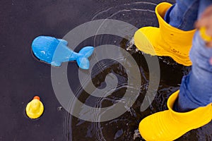 A little attractive girl of five years in a denim suit, yellow boots holds an umbrella and jumps in a puddle