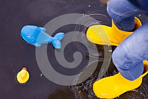 A little attractive girl of five years in a denim suit, yellow boots holds an umbrella and jumps in a puddle