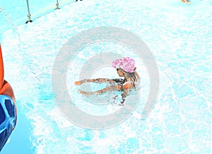 Little Ñaucasian girl in a cap and swimsuit plays in the pool on vacation. Children`s entertainment at sea. Vacation with