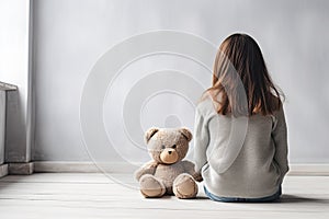 Little autistic girl with teddy bear sitting on floor at empty room. Autism concept