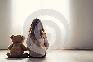 Little autistic girl with teddy bear sitting on floor at empty room. Autism concept