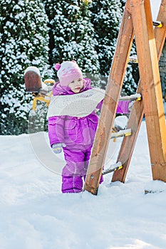 Little babe girl playing on the winter playground.