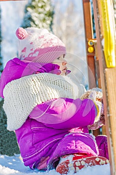 Little babe girl playing on the winter playground.