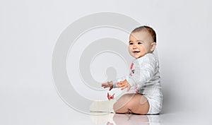 Little babe in gray bodysuit and socks with red bow. She smiling, sitting on the floor isolated on white. Copy space, close up