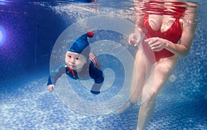 Little baby as elf with mother in red swimming suit swimming underwater