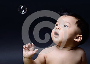 Little baby asian boy drooling and looking soap bubble photo