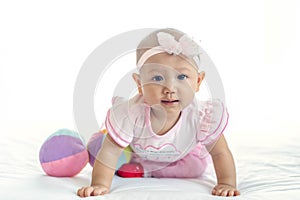 Little baby Asian girl 7 months with pink dress looking at camera on white bed