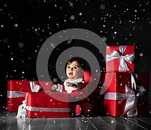 Little baby babe with santa costume with red boxes on a dark background