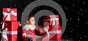 Little baby babe with santa costume with red boxes on a dark background