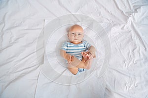 Little baby in bodysuit lying on bed at home coing joyful top view