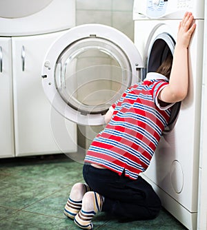 Little baby boy dangerously putting his head into washing machine drum photo