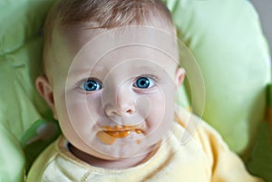 Little baby boy with dirty face eating fruit mash