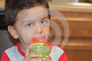 Toddler drinking on his bottle at his home`s kitchen.