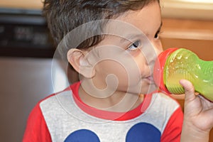 Toddler drinking on his bottle at his home`s kitchen.