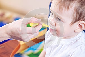 Little baby boy eating on a chair in the kitchen. Mom feeds holding in hand a spoon of porridge