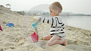 Little baby boy enjoying time on the beach and playing with sand using a shovel. Carefree happiness and fun of a family vacation.