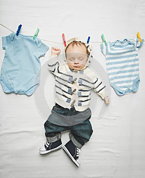 Little baby boy in jeans hanging on cord next to drying clothes