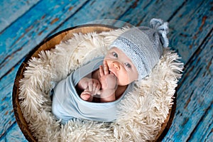 Little baby boy with knitted hat in a basket, happily smiling