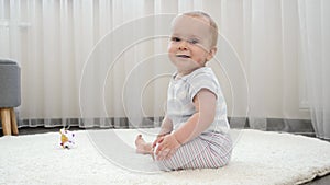 Little baby boy learning sitting up on soft carpet in house. Concept of child development, happy childhood and fun at