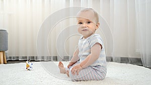 Little baby boy learning sitting up on soft carpet in house. Concept of child development, happy childhood and fun at