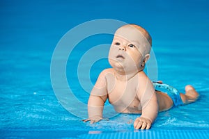 Little baby boy lying in blue swimming pool in water. Activity child