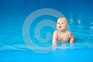 Little baby boy lying in blue swimming pool in water. Activity child