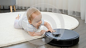 Little baby boy lying on floor and playing with robot vacuum cleaner