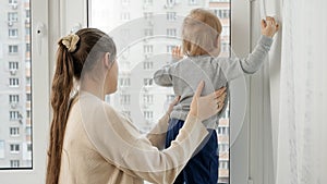 Little baby boy with mother looking out of the window of high store building.