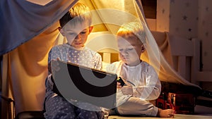 Little baby boy with older brother using tablet computer and watching video in bed before gong to sleep at night