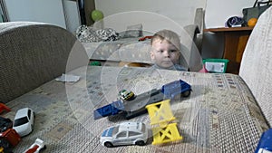 A little baby boy playing with his toys on armchair. Toddler boy is playing with toy cars.