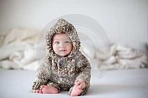 Little baby boy playing at home in bed, dressed in hand made knitted overall