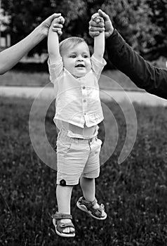 Little baby boy playing outdoor in the grass. Father and mother holding baby hands.