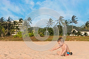 Little baby boy playing on the sand at the background of palm trees and blue sky