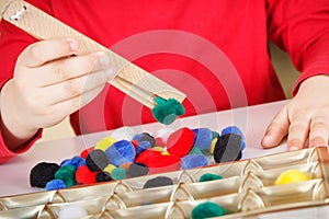 Little baby boy playing with small pompoms and wooden tongs. Development of kids motor skills, coordination and logical thinking