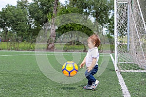 Little baby boy playing soccer on football field.