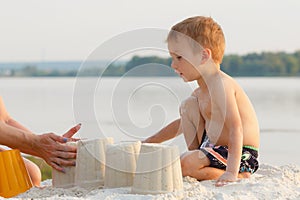 Little baby boy is resting on the sandy shore, build a castle