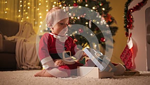 Little baby boy in Santa Claus costume opens Christmas gift box. Families and children celebrating winter holidays.